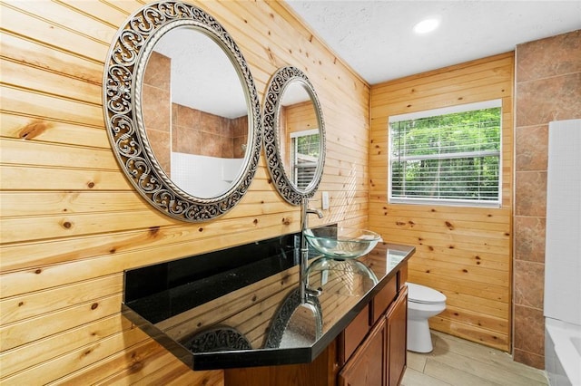 bathroom featuring wood walls, wood-type flooring, a tub to relax in, vanity, and toilet