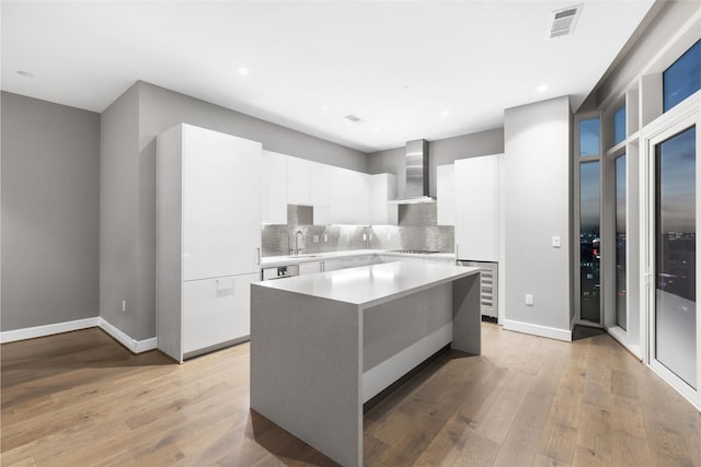 kitchen with white cabinetry, a center island, light hardwood / wood-style floors, sink, and wall chimney exhaust hood