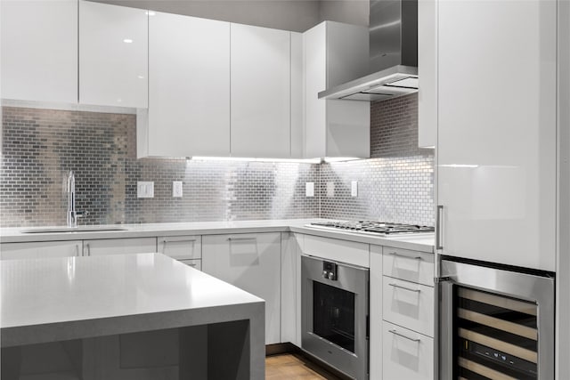 kitchen with appliances with stainless steel finishes, white cabinets, and wall chimney range hood