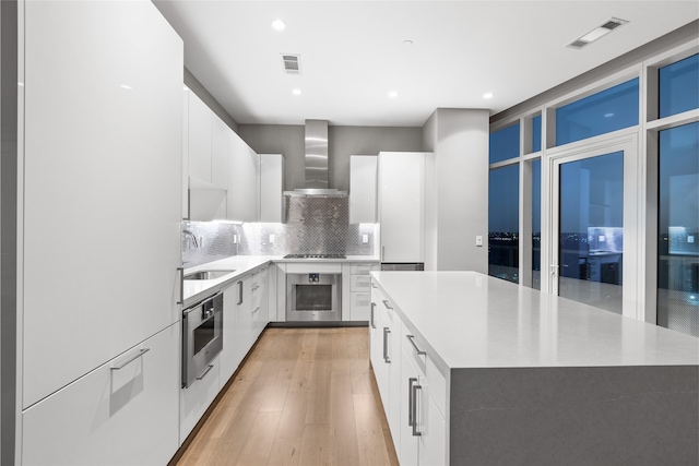 kitchen with a center island, sink, wall chimney exhaust hood, and white cabinets