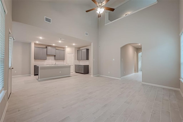 unfurnished living room featuring a high ceiling, light wood-type flooring, and ceiling fan