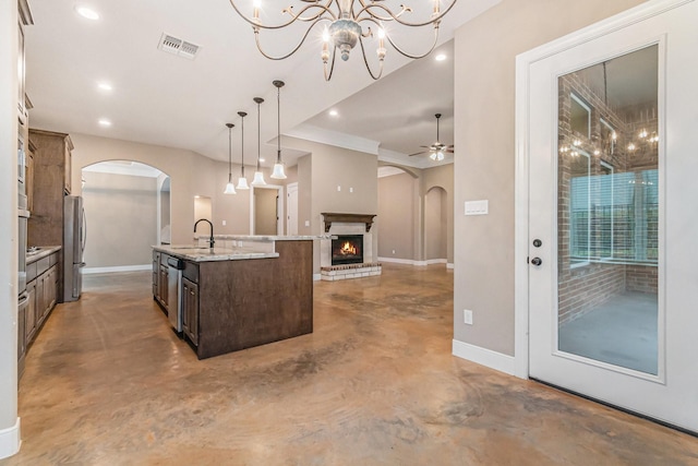 kitchen featuring dark brown cabinetry, decorative light fixtures, concrete floors, appliances with stainless steel finishes, and a kitchen island with sink