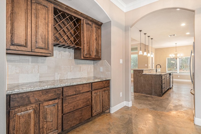 kitchen with pendant lighting, sink, a chandelier, decorative backsplash, and light stone counters