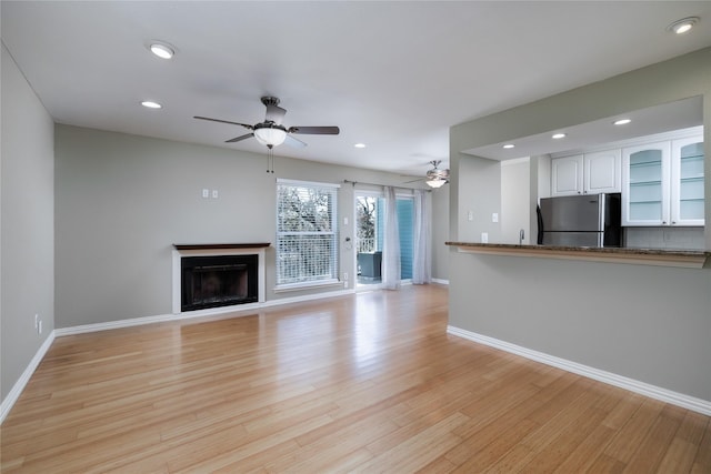 unfurnished living room with ceiling fan, baseboards, and a fireplace