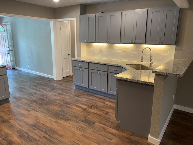 kitchen featuring gray cabinets, stone countertops, sink, dark hardwood / wood-style flooring, and decorative backsplash