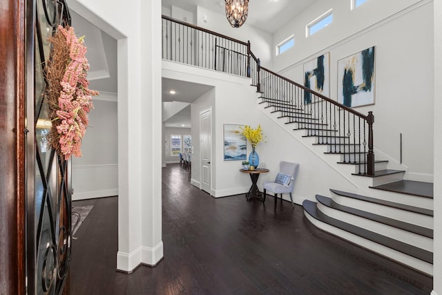 entryway featuring an inviting chandelier, a towering ceiling, plenty of natural light, and dark hardwood / wood-style floors