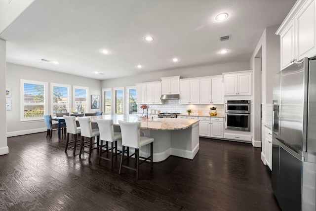 kitchen featuring a kitchen bar, white cabinetry, tasteful backsplash, an island with sink, and stainless steel appliances