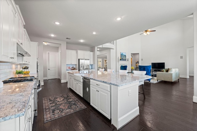 kitchen featuring a large island with sink, appliances with stainless steel finishes, white cabinets, and backsplash