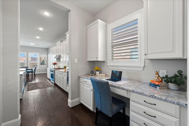 kitchen featuring white cabinetry, high end range, built in desk, dark hardwood / wood-style flooring, and light stone countertops