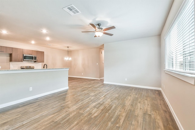 unfurnished living room featuring sink, ceiling fan with notable chandelier, and hardwood / wood-style floors