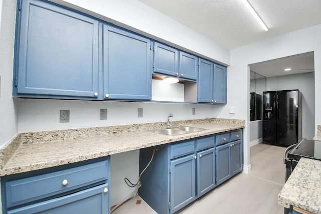 kitchen featuring black fridge, sink, a textured ceiling, and blue cabinetry