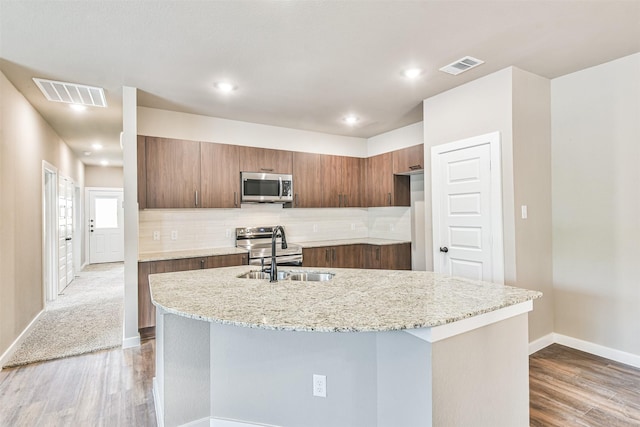 kitchen with tasteful backsplash, a kitchen island with sink, sink, and hardwood / wood-style floors