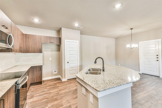 kitchen featuring sink, light stone counters, appliances with stainless steel finishes, an island with sink, and pendant lighting