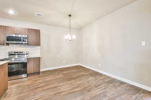 kitchen with appliances with stainless steel finishes, pendant lighting, backsplash, dark hardwood / wood-style flooring, and a notable chandelier