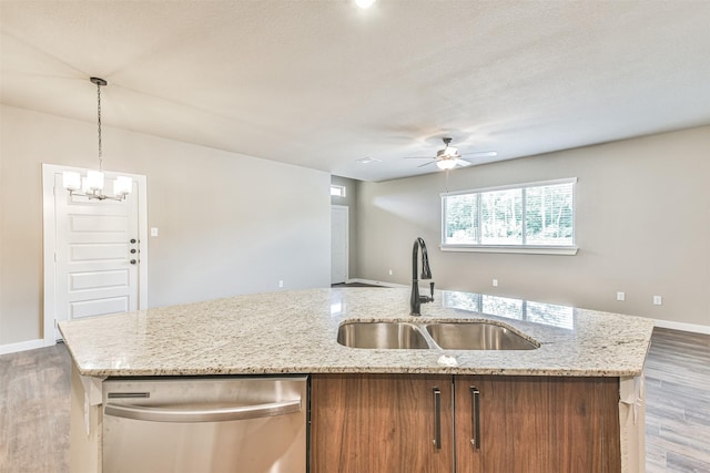 kitchen with sink, a kitchen island with sink, hanging light fixtures, light stone counters, and stainless steel dishwasher