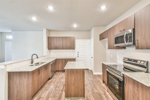 kitchen with sink, light hardwood / wood-style flooring, appliances with stainless steel finishes, a kitchen island, and kitchen peninsula