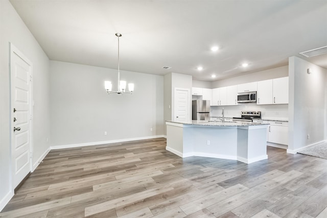 kitchen featuring white cabinetry, hanging light fixtures, appliances with stainless steel finishes, light stone countertops, and a kitchen island with sink