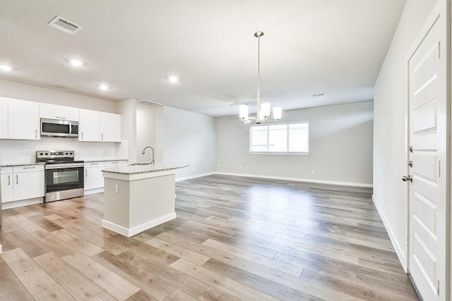 kitchen featuring white cabinetry, decorative light fixtures, stainless steel appliances, light stone countertops, and a kitchen island with sink