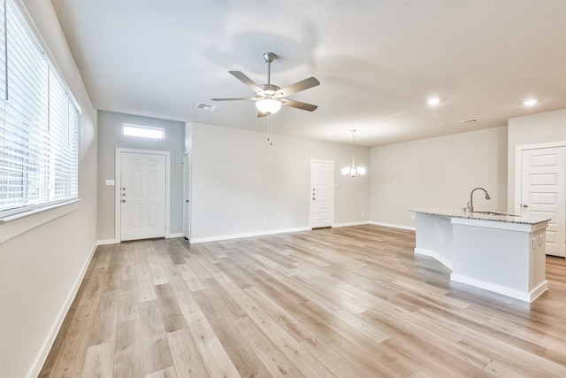 unfurnished living room with sink, ceiling fan with notable chandelier, and light hardwood / wood-style flooring