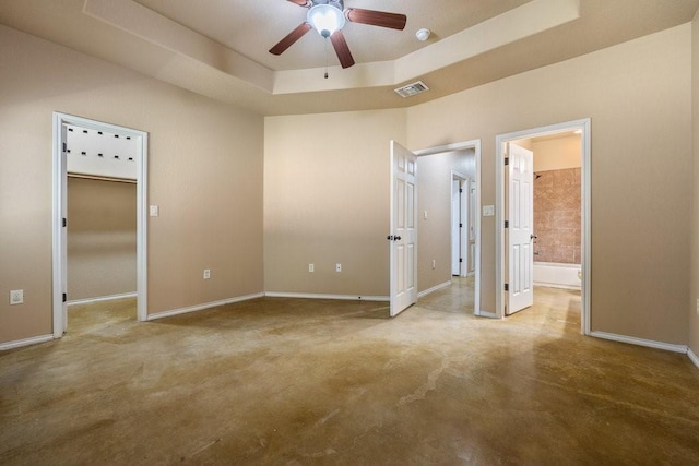 unfurnished bedroom with ceiling fan, a tray ceiling, and ensuite bath