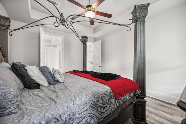 bedroom featuring ceiling fan, a tray ceiling, and light wood-type flooring