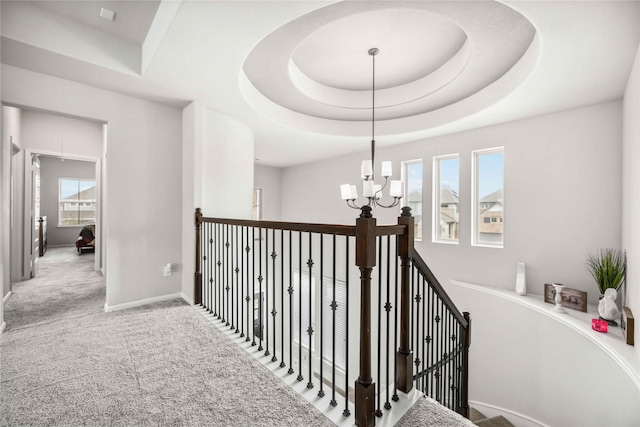 hallway with carpet flooring, a raised ceiling, and a notable chandelier