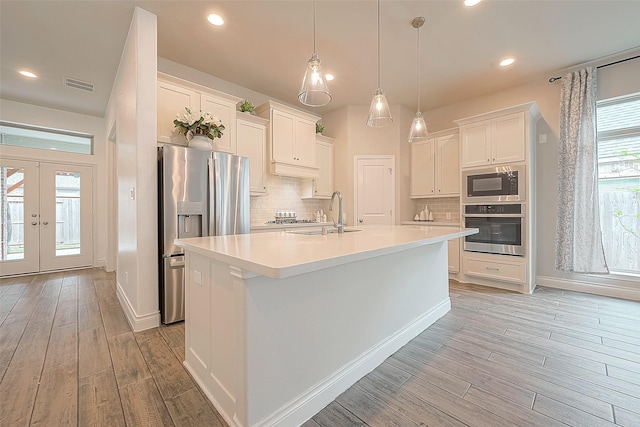 kitchen with white cabinetry, sink, decorative backsplash, stainless steel appliances, and a center island with sink