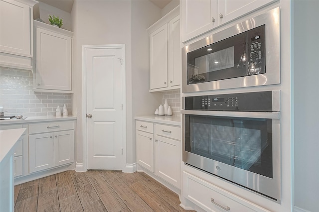 kitchen featuring built in microwave, stainless steel oven, backsplash, and white cabinets