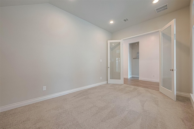 carpeted spare room with vaulted ceiling and french doors