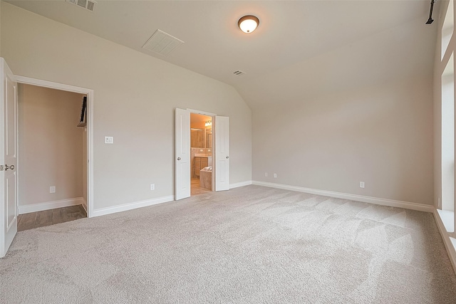 unfurnished bedroom with vaulted ceiling, carpet, and ensuite bathroom