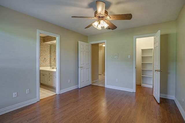 unfurnished bedroom featuring connected bathroom, a spacious closet, a closet, ceiling fan, and light hardwood / wood-style floors