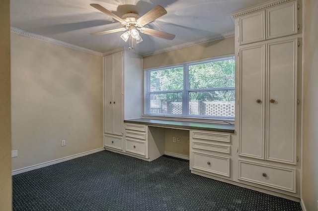 unfurnished office with crown molding, dark carpet, built in desk, and ceiling fan