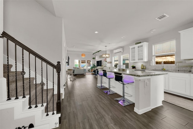 kitchen with white cabinetry, a kitchen island, a wall mounted AC, tasteful backsplash, and a kitchen bar