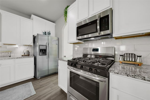 kitchen with stainless steel appliances, light stone countertops, white cabinets, and light hardwood / wood-style flooring