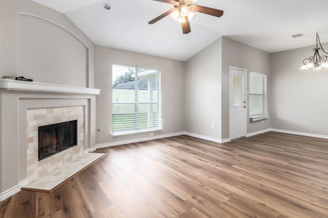 unfurnished living room featuring lofted ceiling, hardwood / wood-style flooring, ceiling fan with notable chandelier, and a tile fireplace