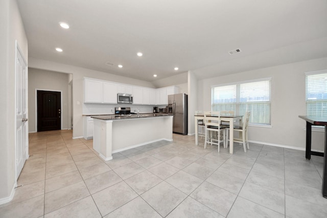 kitchen featuring white cabinets, a kitchen breakfast bar, light tile patterned floors, stainless steel appliances, and a center island with sink