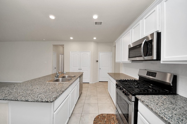 kitchen featuring sink, white cabinets, light tile patterned floors, stainless steel appliances, and a center island with sink