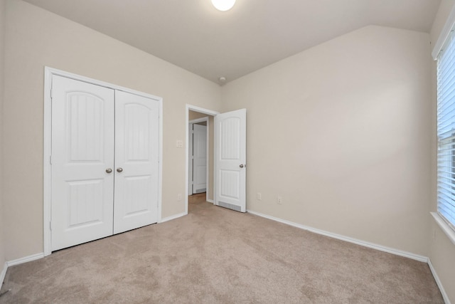 unfurnished bedroom featuring lofted ceiling, light carpet, and a closet