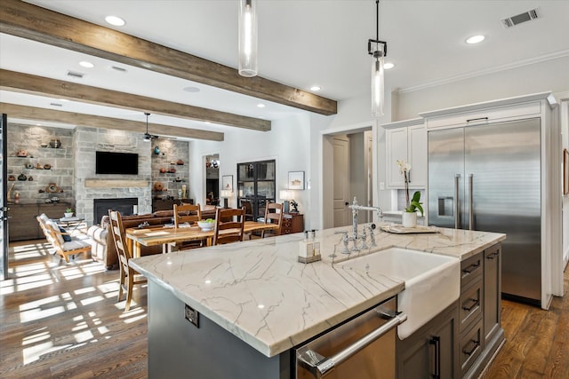 kitchen with appliances with stainless steel finishes, dark hardwood / wood-style floors, a stone fireplace, an island with sink, and hanging light fixtures