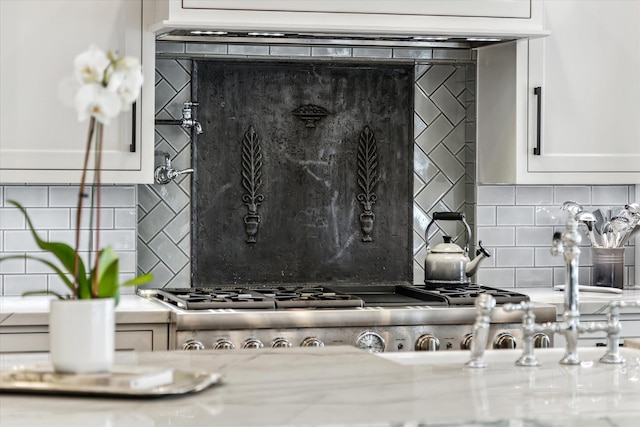 details featuring tasteful backsplash, white cabinetry, and light stone countertops