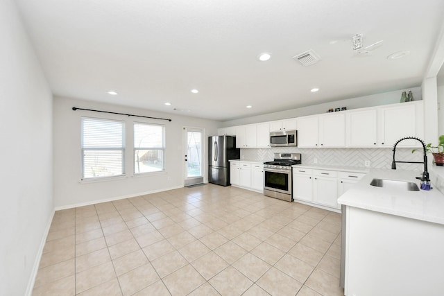 kitchen with light tile patterned flooring, appliances with stainless steel finishes, white cabinetry, sink, and decorative backsplash