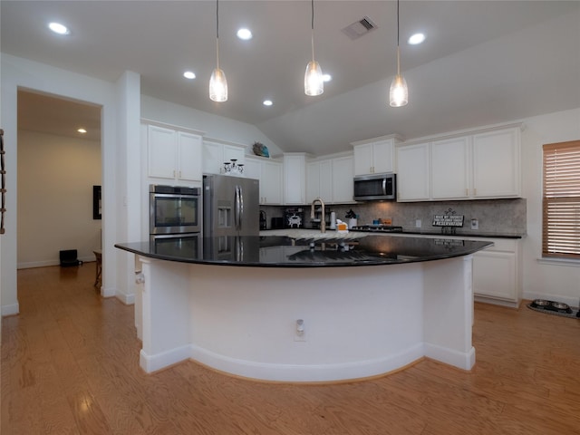 kitchen featuring stainless steel appliances, vaulted ceiling, white cabinets, and a large island with sink