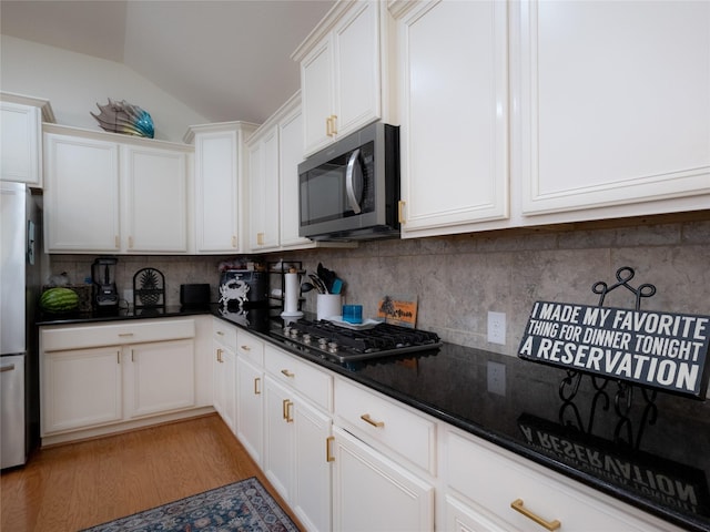 kitchen featuring white cabinetry, tasteful backsplash, light hardwood / wood-style flooring, dark stone countertops, and stainless steel appliances