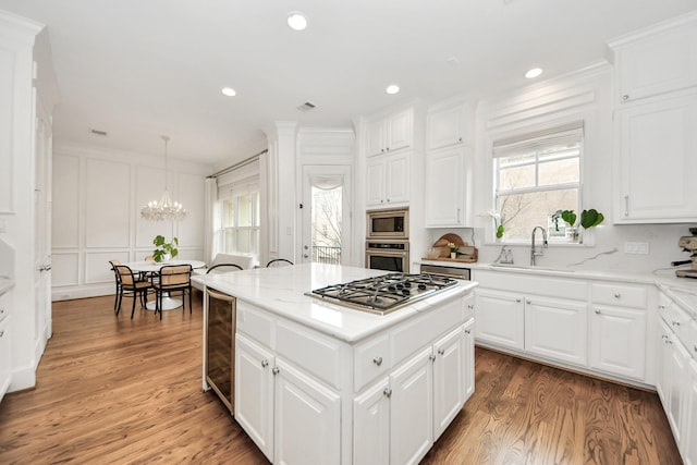 kitchen with sink, hanging light fixtures, a kitchen island, stainless steel appliances, and white cabinets