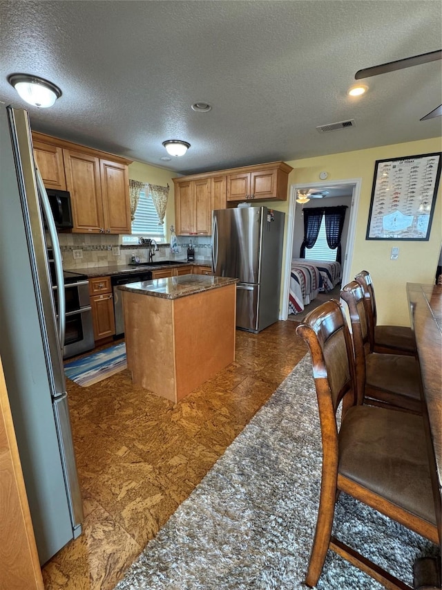 kitchen with appliances with stainless steel finishes, backsplash, dark stone counters, a center island, and a textured ceiling