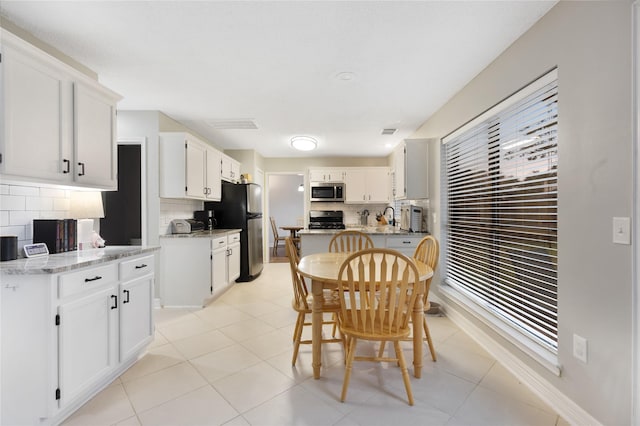 kitchen featuring stainless steel appliances, white cabinetry, light stone countertops, and tasteful backsplash