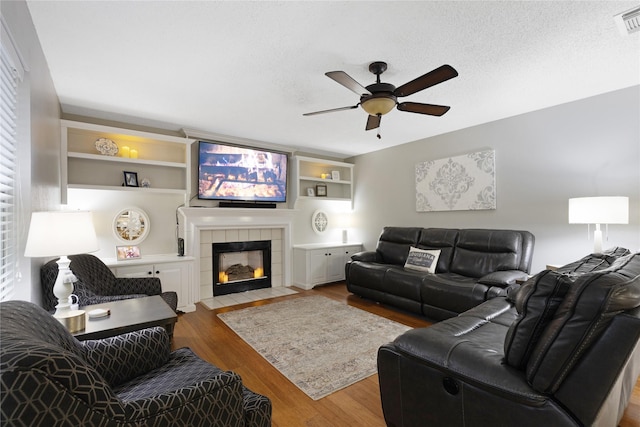 living room with light hardwood / wood-style flooring, a textured ceiling, built in features, ceiling fan, and a fireplace