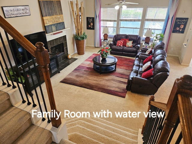 living room with a tile fireplace, ceiling fan, and carpet flooring