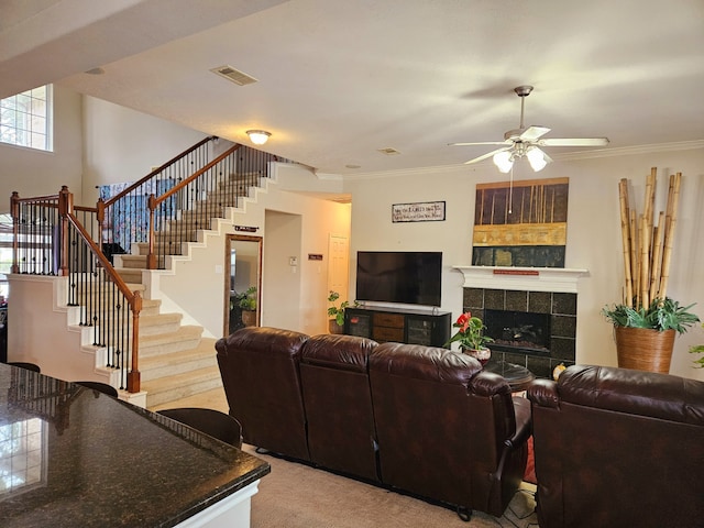 carpeted living room featuring crown molding, ceiling fan, and a tiled fireplace