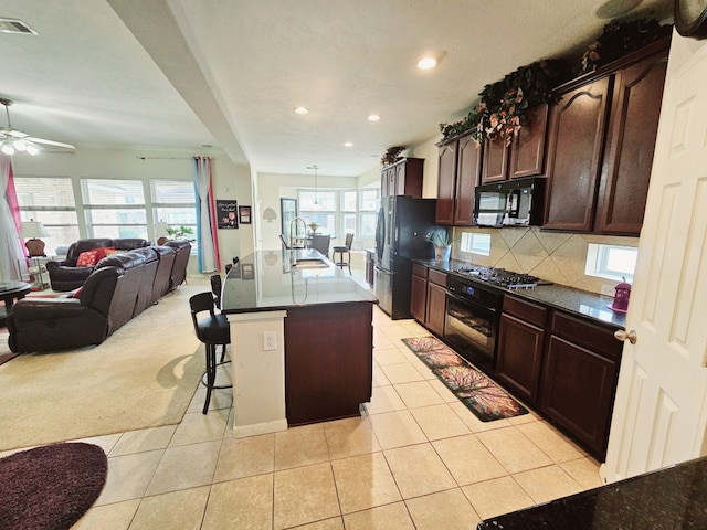 kitchen featuring sink, a kitchen breakfast bar, a kitchen island with sink, decorative backsplash, and black appliances